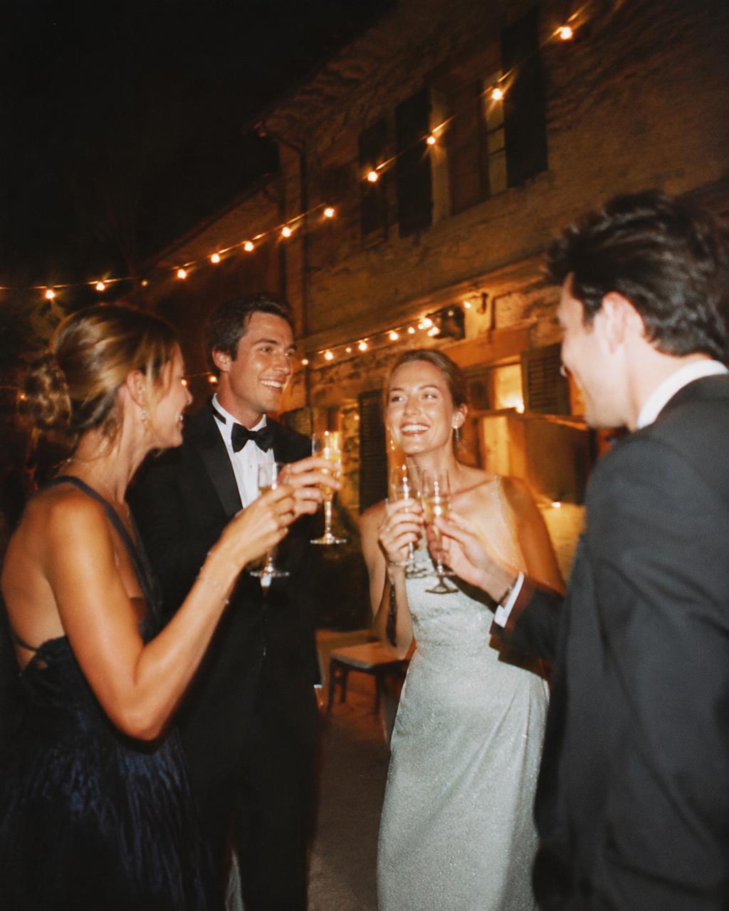 Four friends in black tie toasting under string lights
