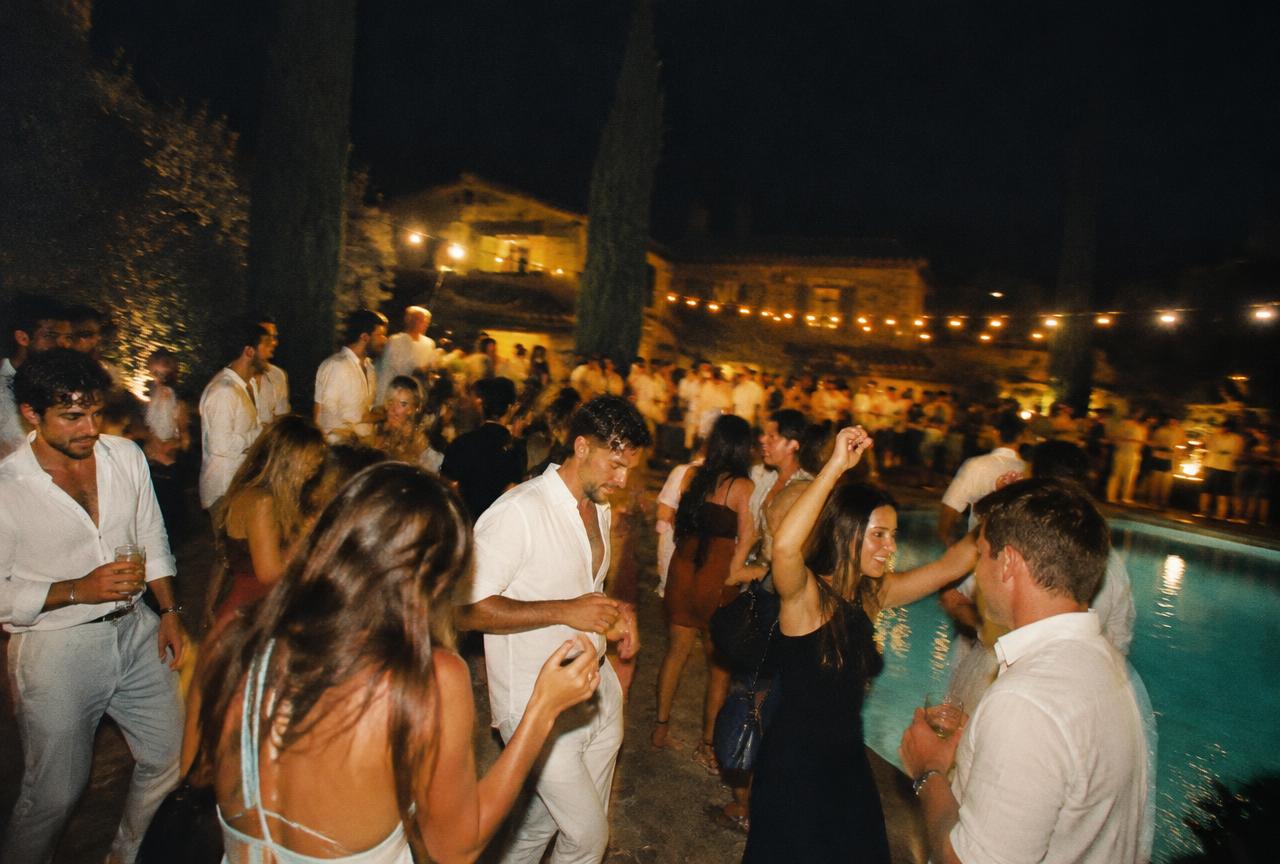 Guests in linen dancing beside a lit pool under string lights