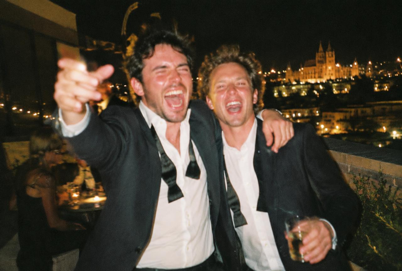 Two men in loosened bow ties shouting with joy on a rooftop