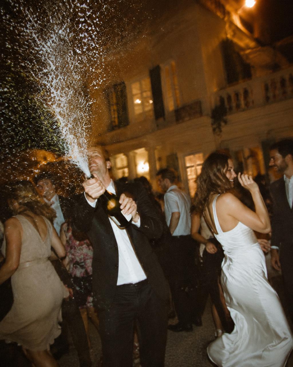 Champagne sprayed above dancing guests in front of a villa
