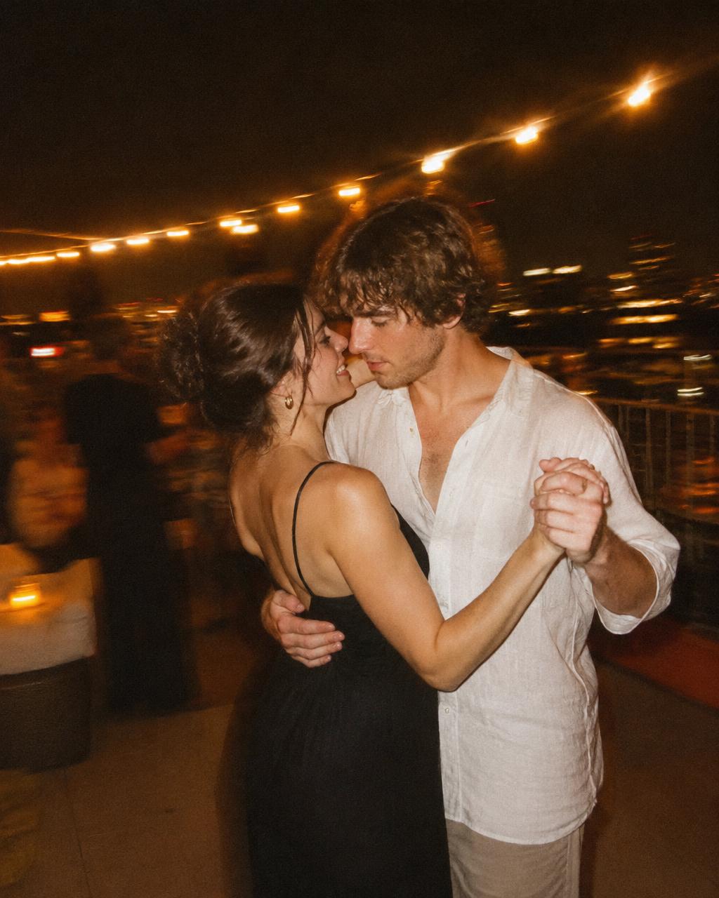 A couple slow dancing under string lights on a rooftop