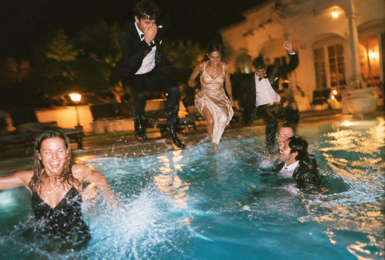 Guests in tuxedos and gowns jumping into a pool at night