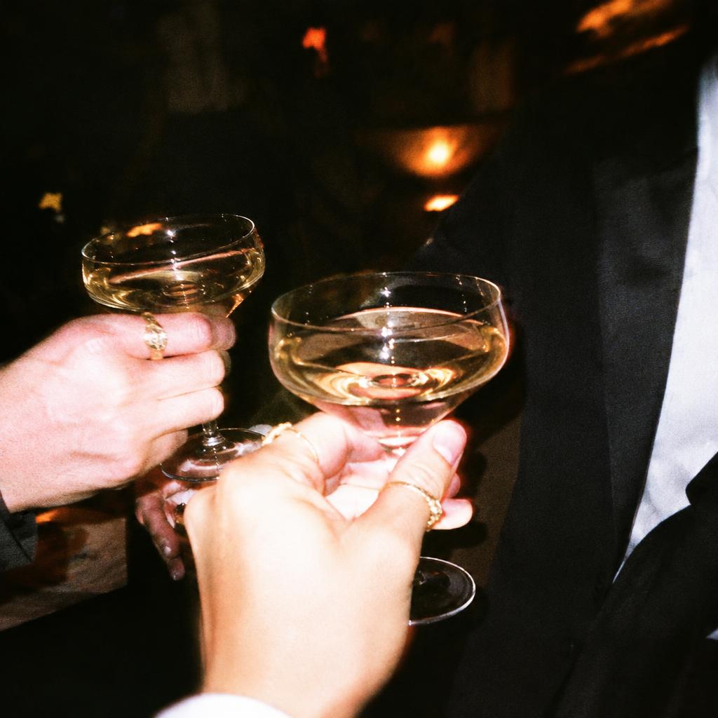 Two hands with gold rings clinking champagne coupes