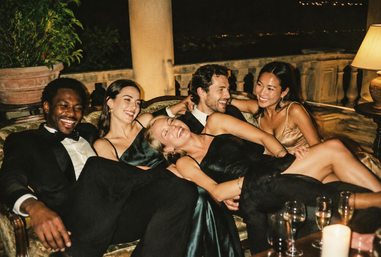 Friends in evening wear piled on a vintage sofa on a terrace