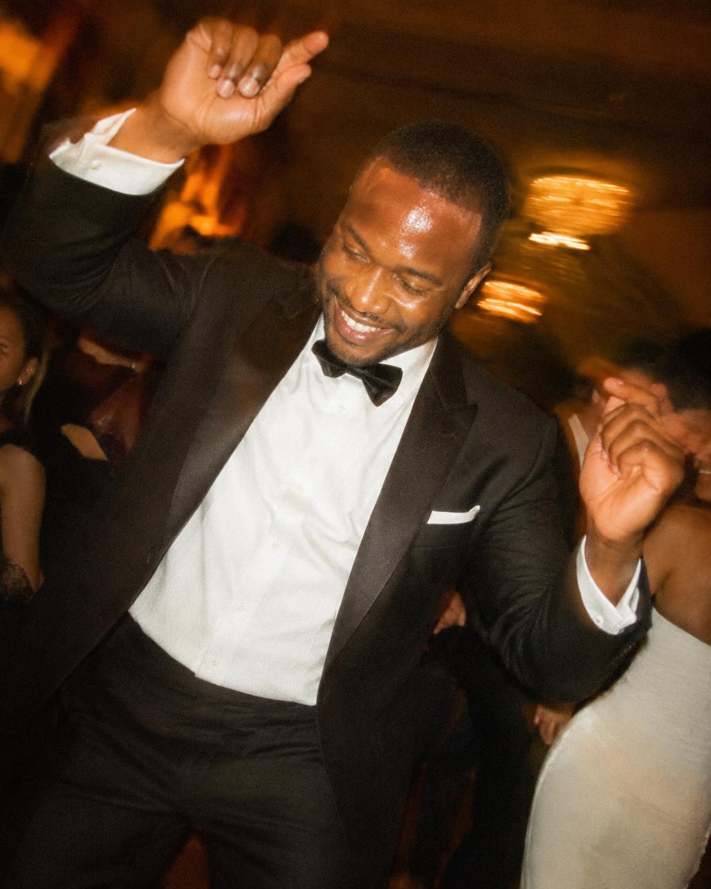 A man in a tuxedo dancing with his arms raised