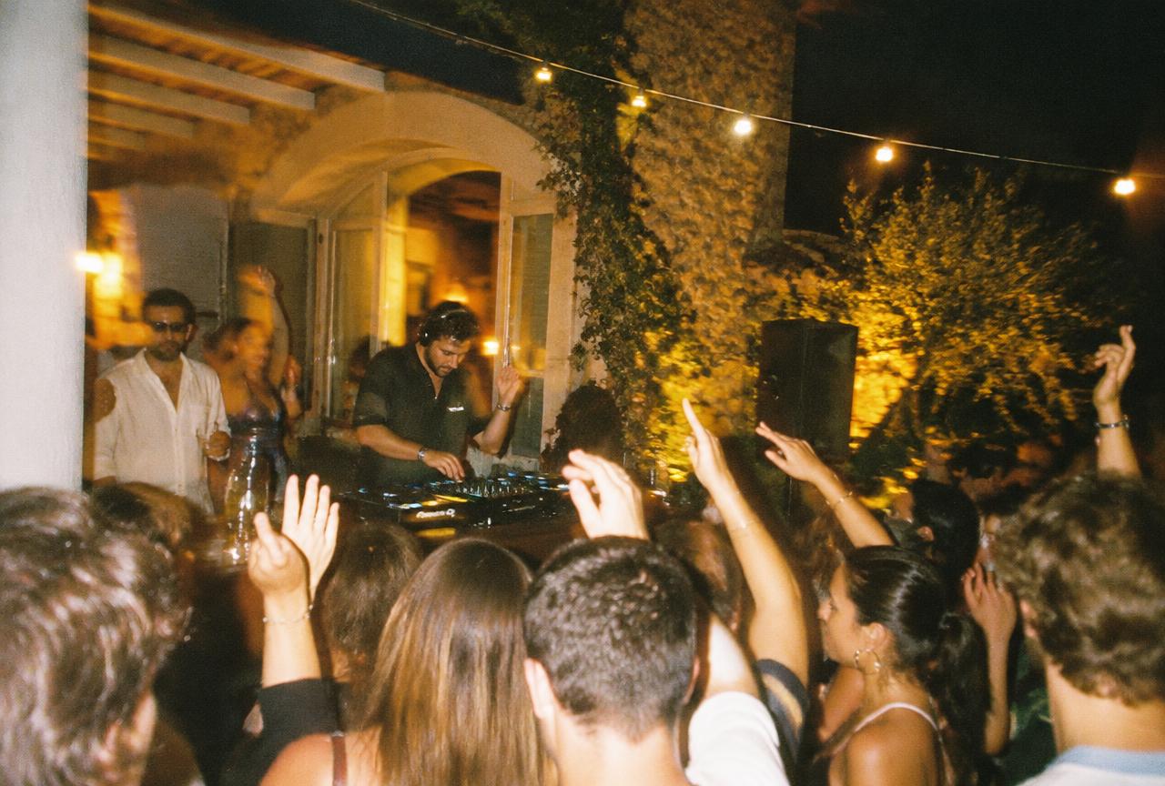 A crowd with hands up in front of a DJ in a villa courtyard