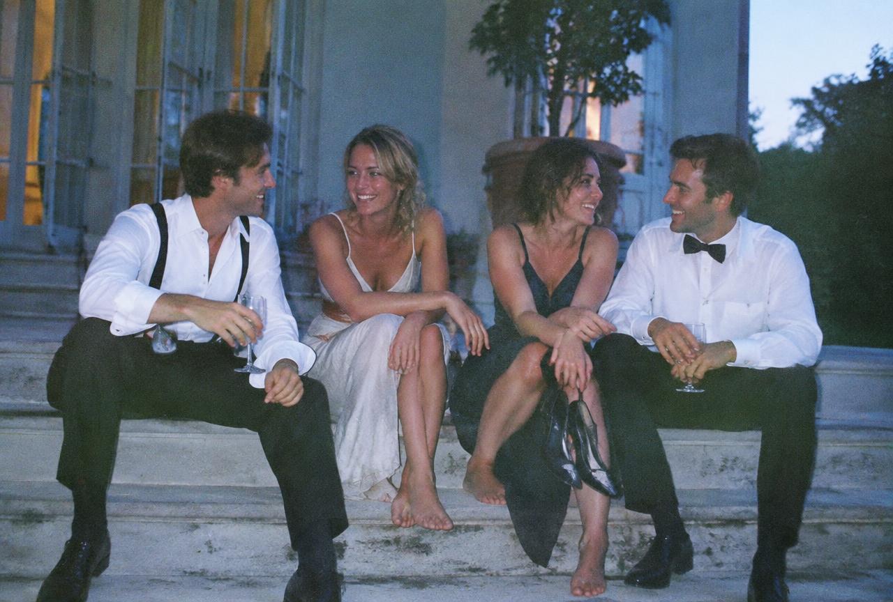Friends in rumpled evening wear on villa steps at dawn